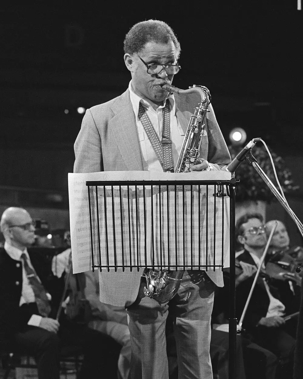 Dexter Gordon toca el saxo tenor dret darrere d’un faristol, amb l’orquestra asseguda al fons