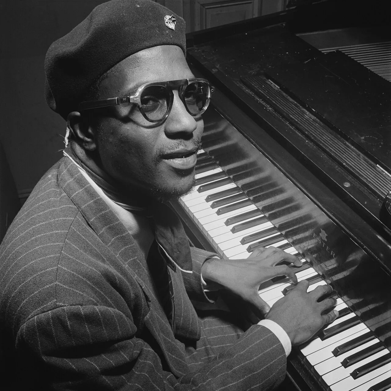 Thelonious Monk assegut al piano, amb boina i ulleres, mira la càmera